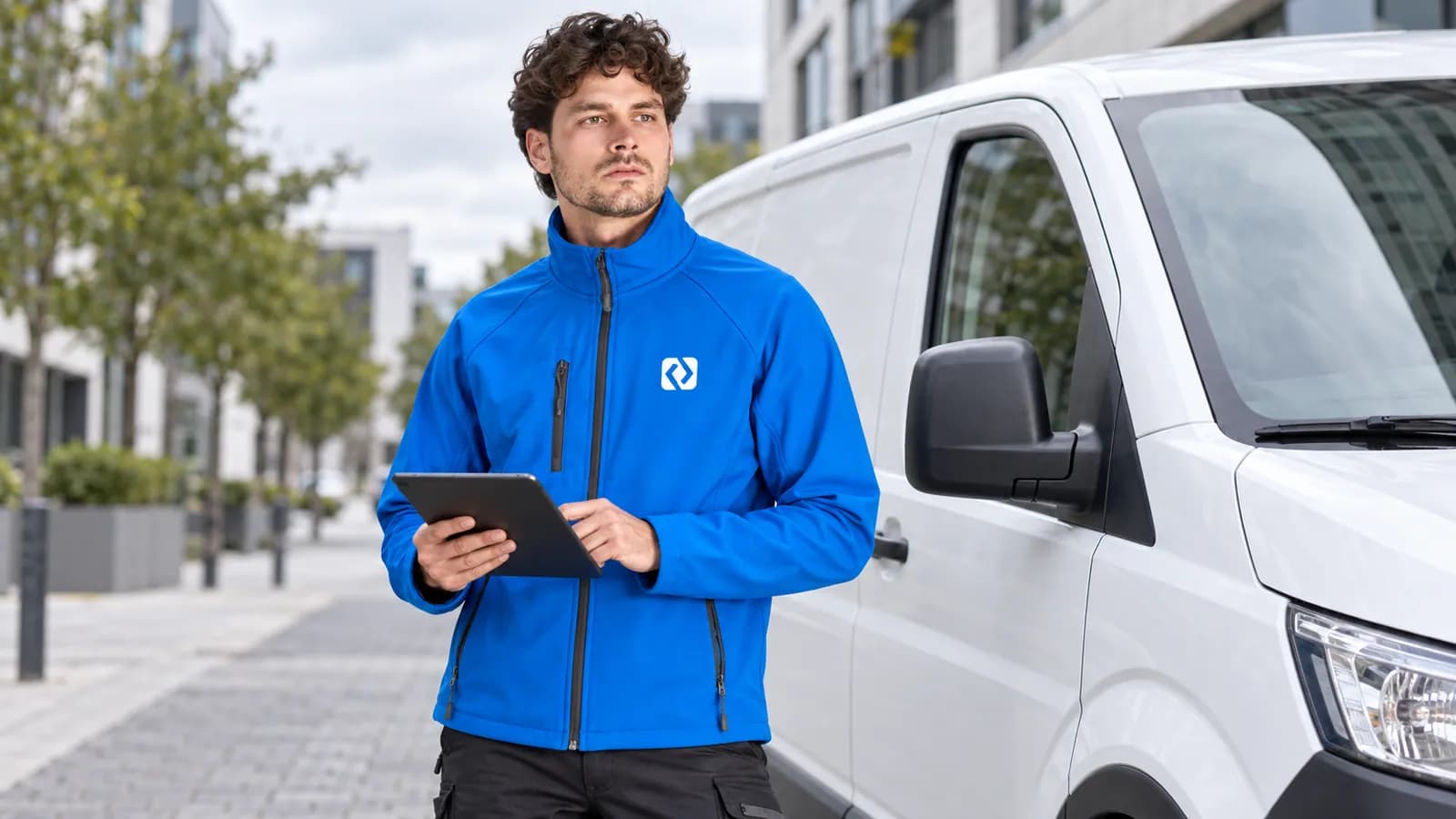 Servisný technik v modrej softshellovej bunde s logom na hrudi pri dodávke
